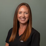 Professional headshot of a smiling female dental team member in black scrubs against a neutral background.