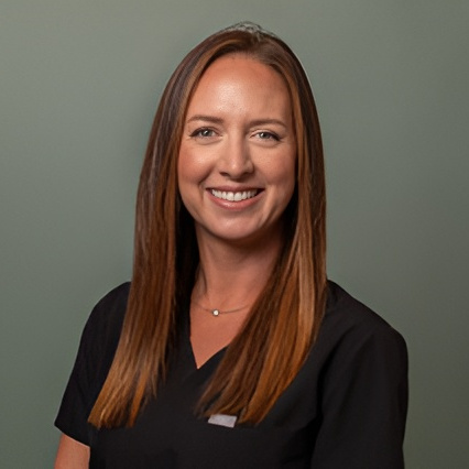 Professional headshot of a smiling female dental team member in black scrubs against a neutral background.