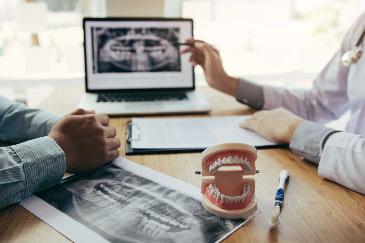 Dentists are discussing dental problems at report x-ray image on laptop screen to patients.