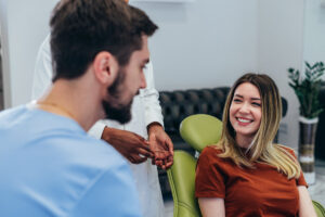 Male dentist in dental office talking with female patient and preparing her for treatment. Explaining the procedure of new dental implants. Focus on a beautiful blonde patient woman.