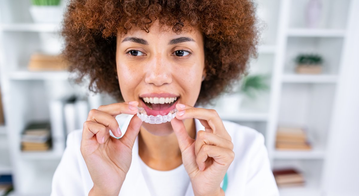 Woman smiling while holding a clear Invisalign aligner